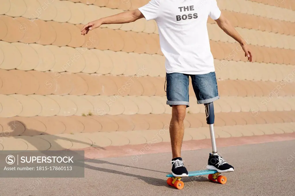 Young man with artificial limb and foot standing on skateboard at sports court