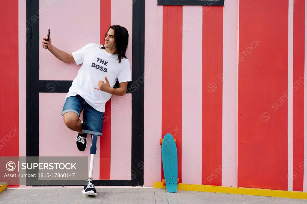 Disabled man taking selfie while standing against red wall