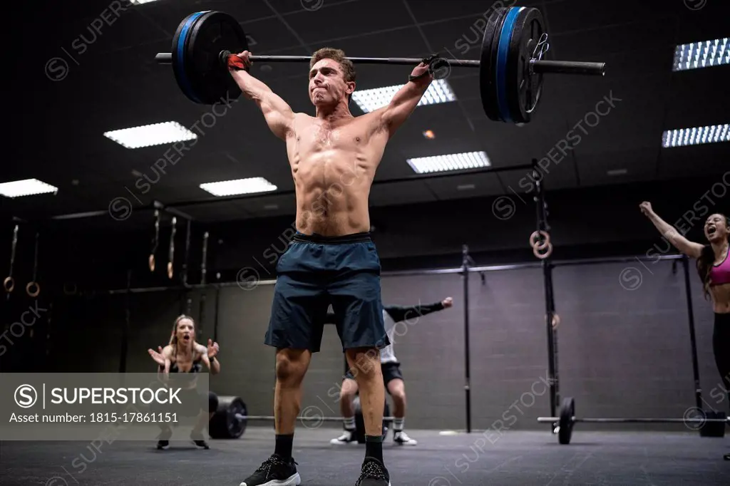 Amputee athlete picking barbell with people cheering in background at gym