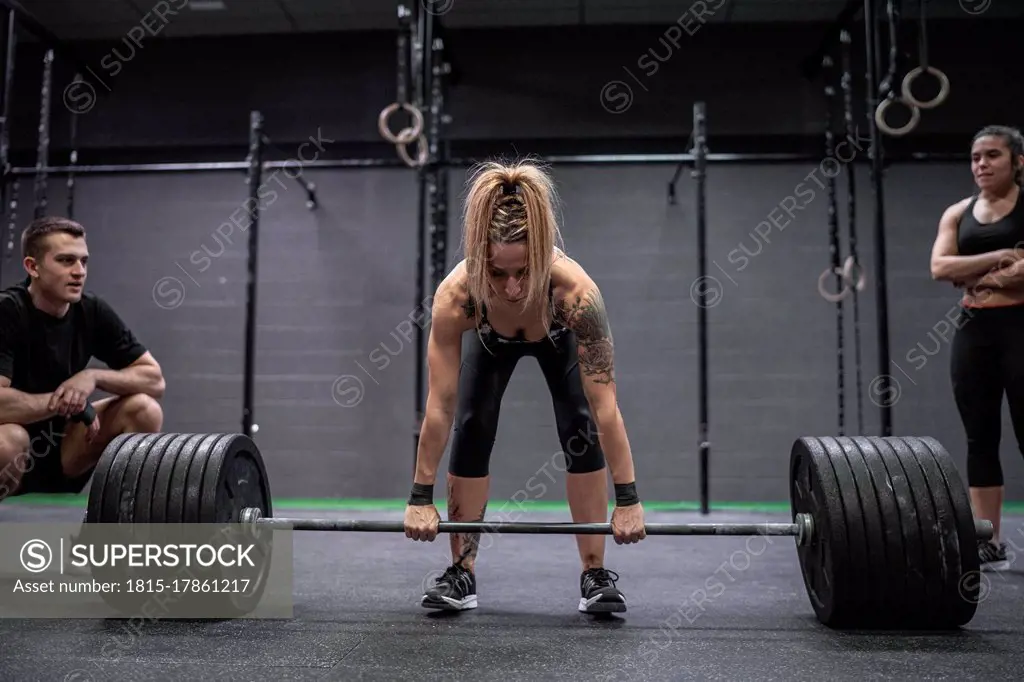 Athletes watching woman picking barbell while standing in gym