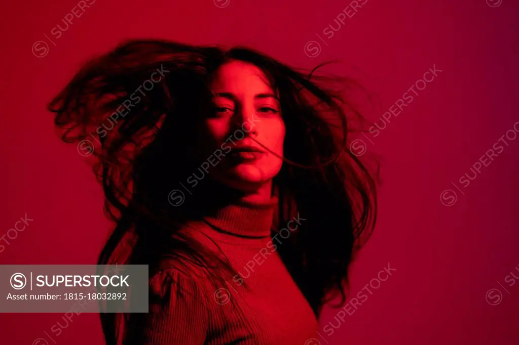 Mid adult woman staring while tossing hair against red background