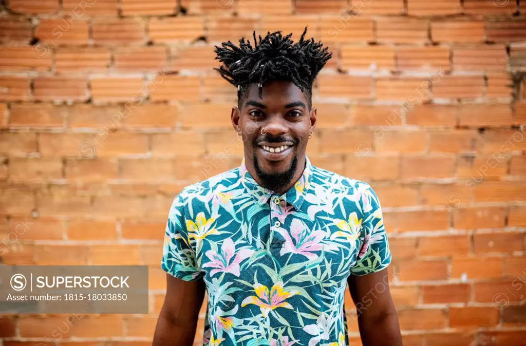 Smiling mid adult man with locs standing against brick wall in city