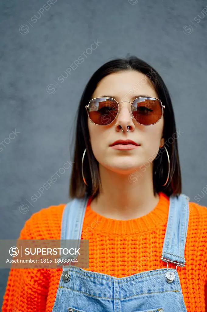 Young woman wearing sunglasses standing against gray wall