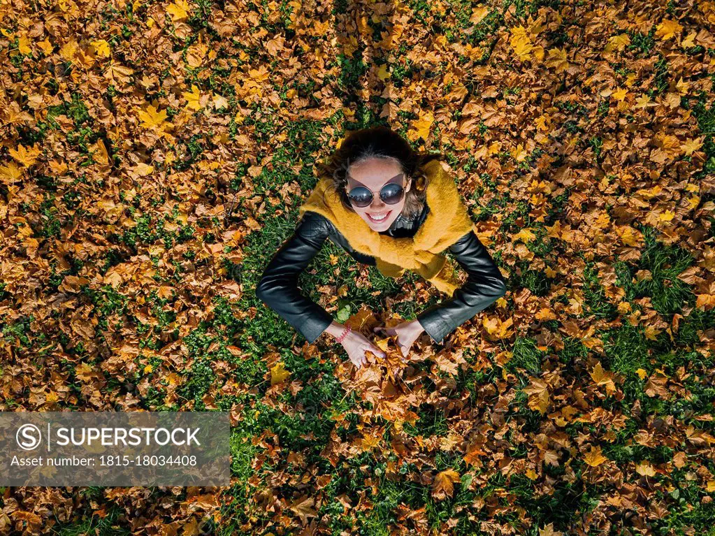 Happy woman holding dry leaves while enjoying at park during autumn