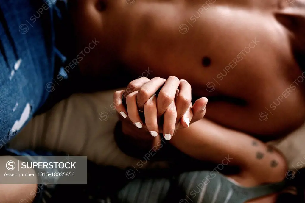 Couple holding hands while lying on bed