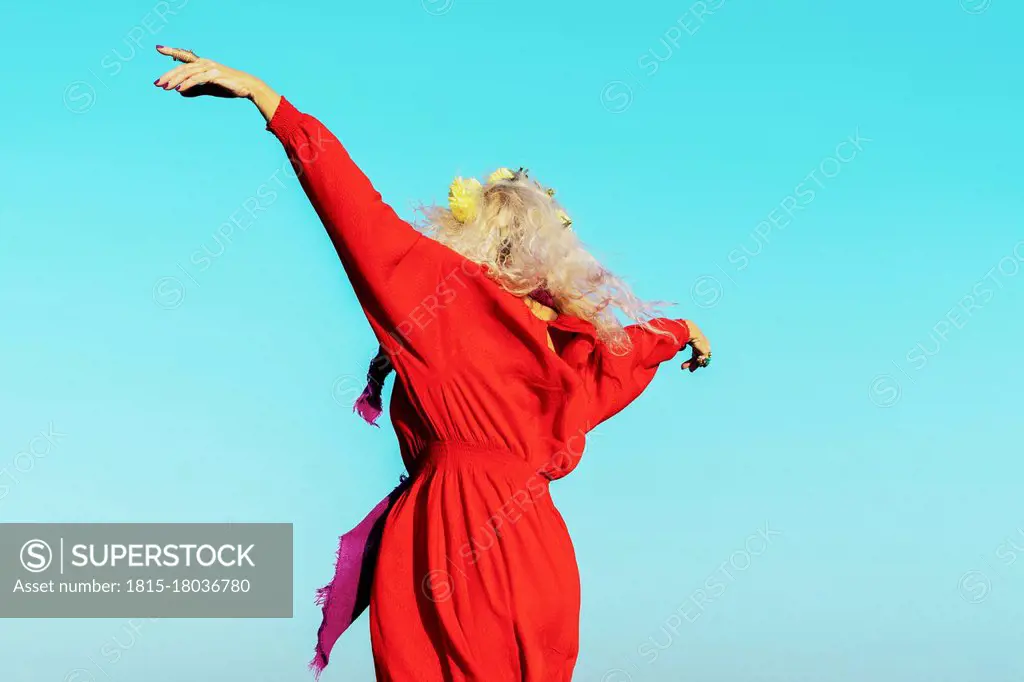 Carefree woman with arms outstretched against blue sky on sunny day