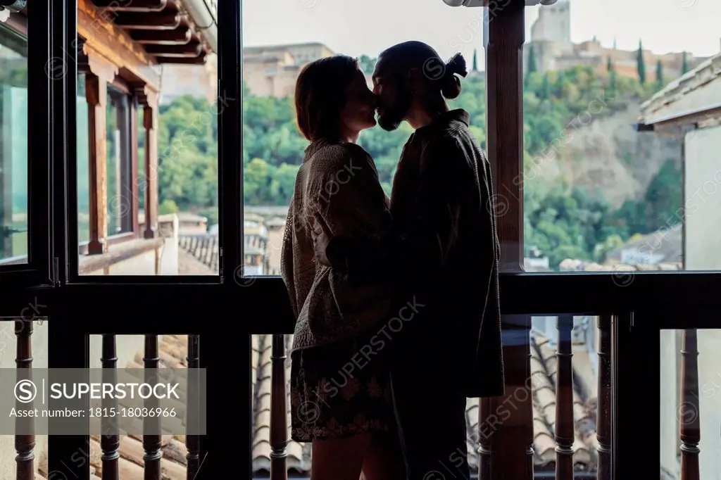 Couple kissing while standing by window at home