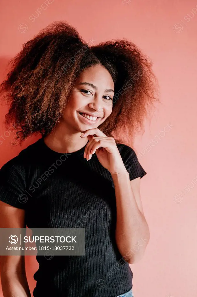 Smiling Afro woman with hand on chin standing against peach background