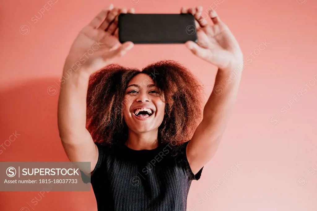 Cheerful Afro woman taking selfie through mobile phone against peach background