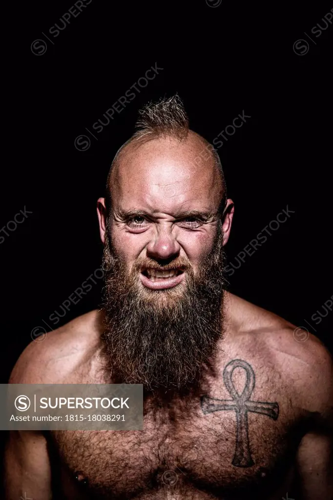 Frustrated male hipster clenching teeth against black background