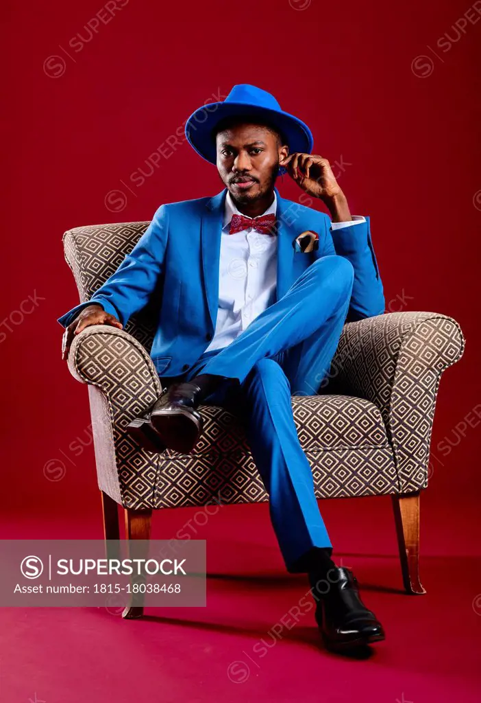 Confident man wearing blue suit sitting on chair against red background