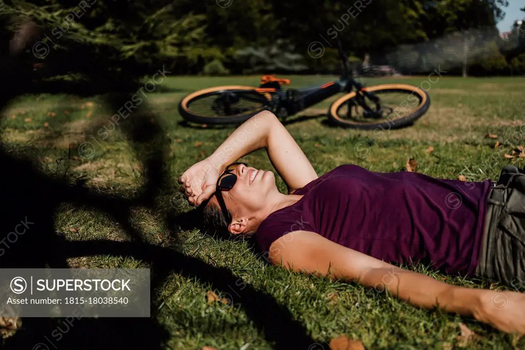 Woman lying on grass while resting by mountain bike at park