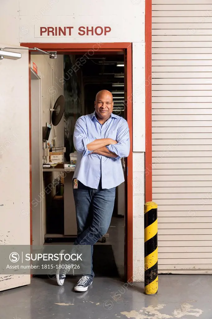 Smiling supervisor with arms crossed leaning on doorway at print shop