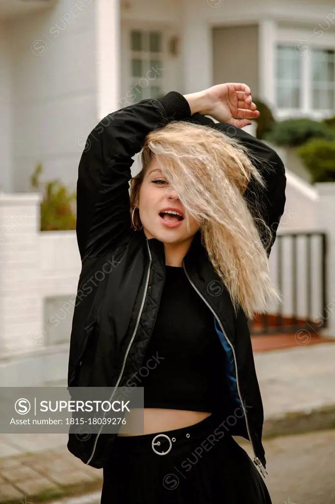 Blond hipster woman with arms raised standing on street