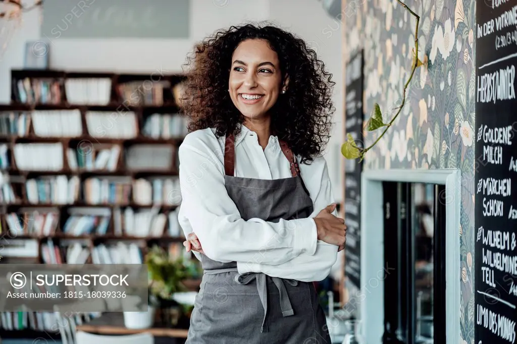 Young entrepreneur wearing apron looking away while standing at cafe