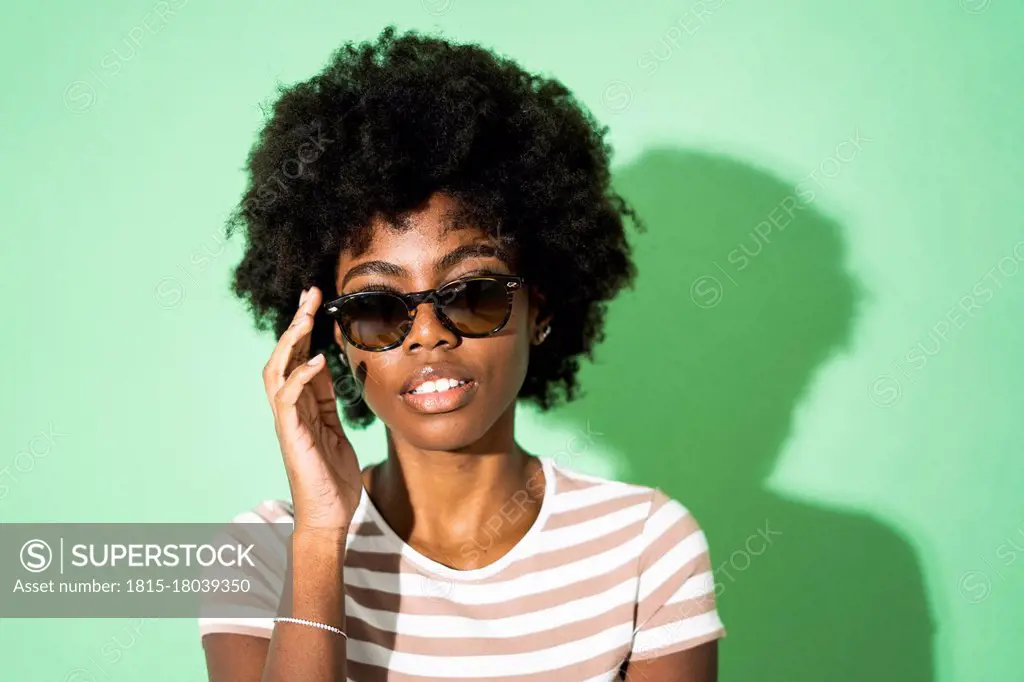 Woman adjusting sunglasses while standing against green background