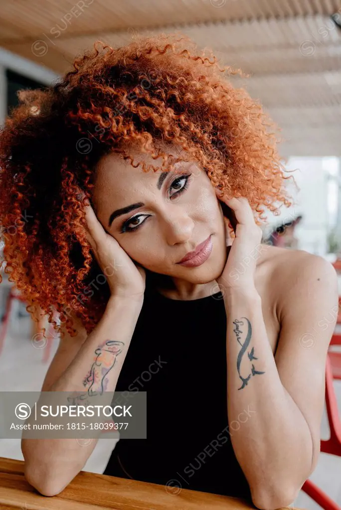 Confident mid adult woman with tattoo leaning on table in cafe