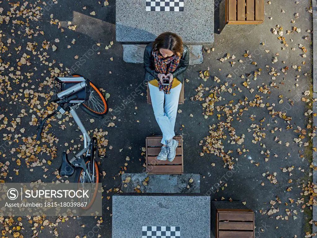 Woman using smart phone while sitting amidst chess tables in park during autumn