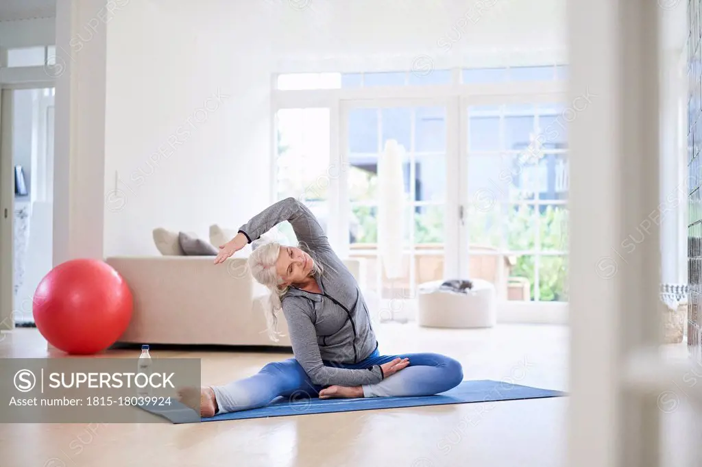 Senior woman stretching arms while exercising in living room