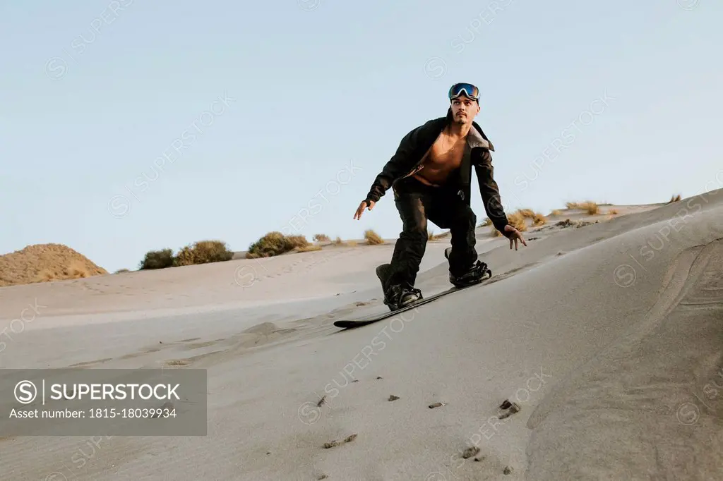 Young man looking away while sandboarding against clear sky at Almeria, Tabernas desert, Spain