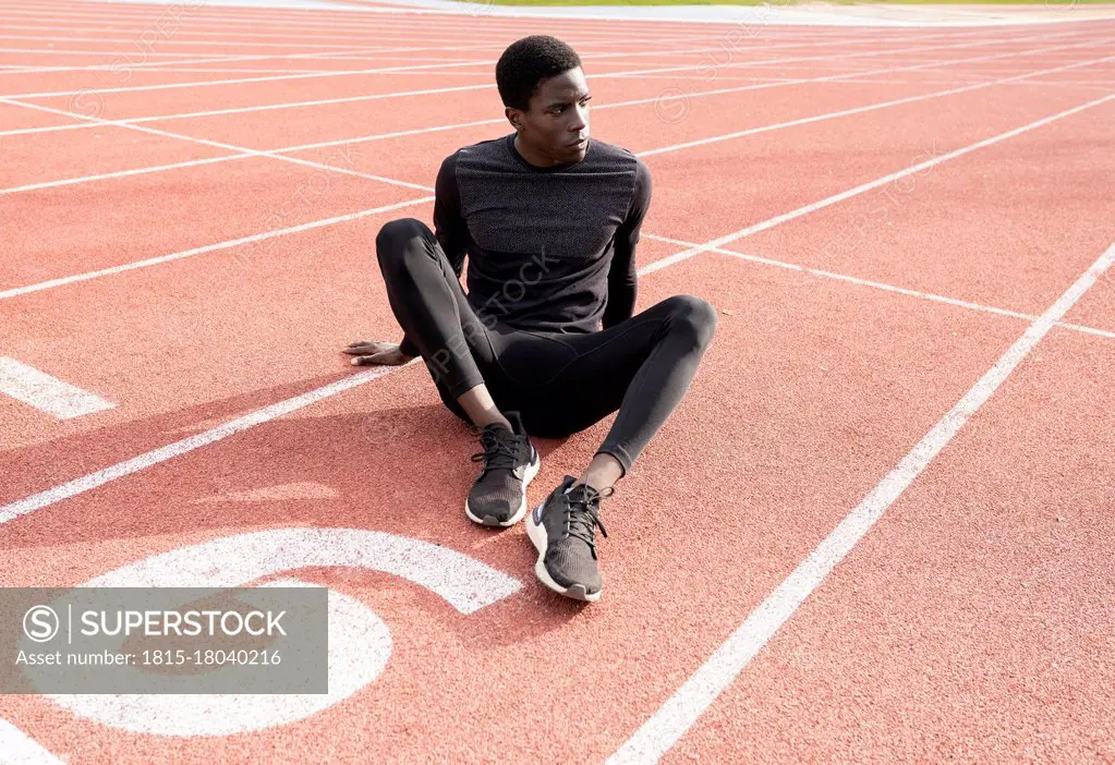 Sportsman contemplating while sitting on running track during sunny day