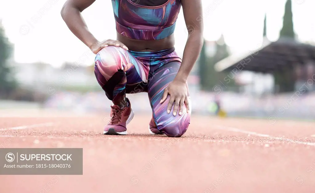 Young female sportsperson kneeling on starting line at running track