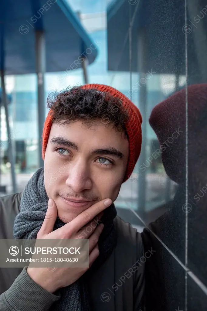 Thoughtful man with hand on chin standing by black wall