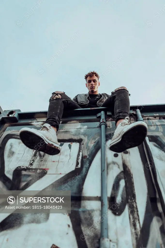 Fashionable young man on metal container against sky