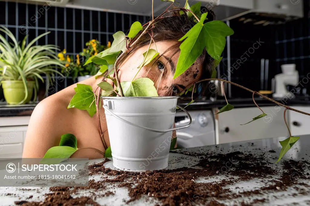 Young woman face covered with leaf and flower pot at home