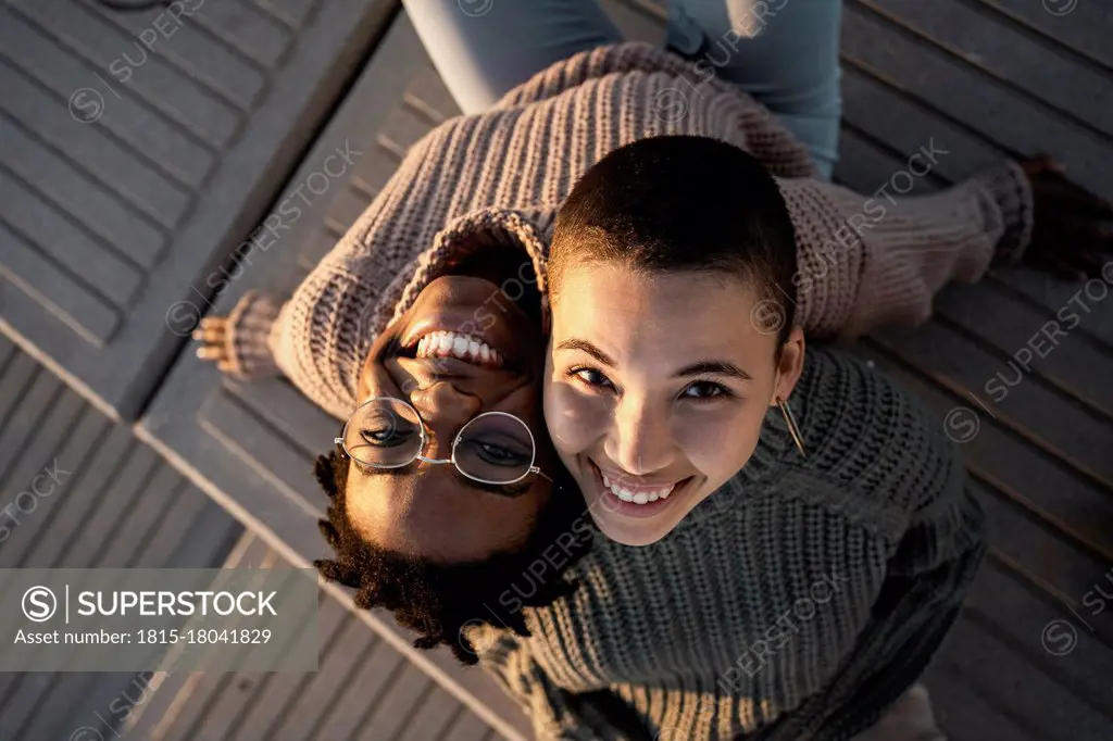 Smiling friends leaning on each other shoulder while sitting on bench