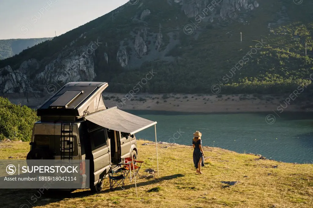 Woman looking at lake while standing by camper van during vacation