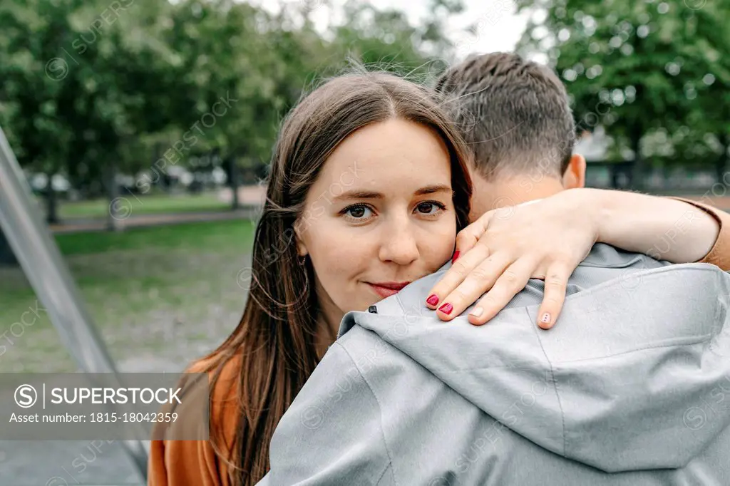 Smiling girlfriend embracing boyfriend in public park