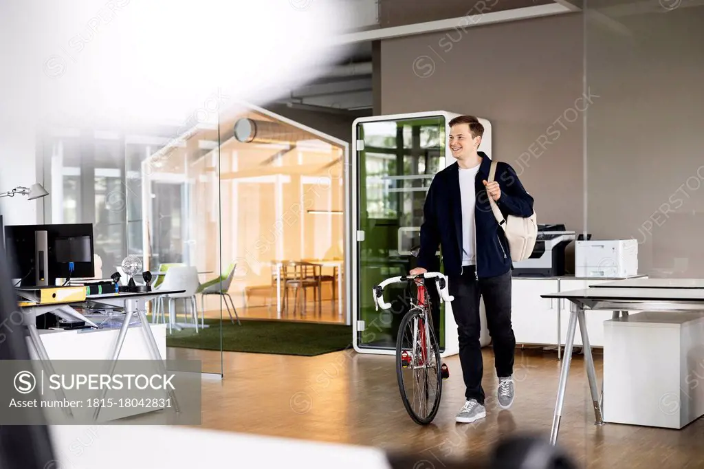 Smiling businessman walking with bicycle at open plan office