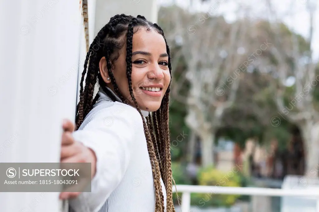 Smiling woman stretching hand while leaning on wall