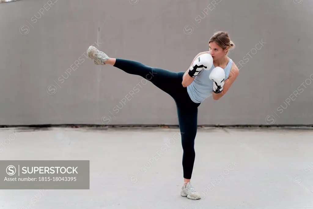 Woman with boxing glove practicing kickboxing against wall