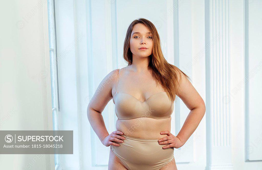 Confident curvy model in beige lingerie with hand on hip standing