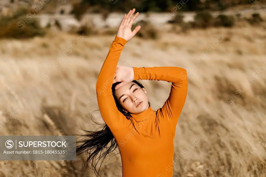 Beautiful woman with arms raised standing in field during windy day