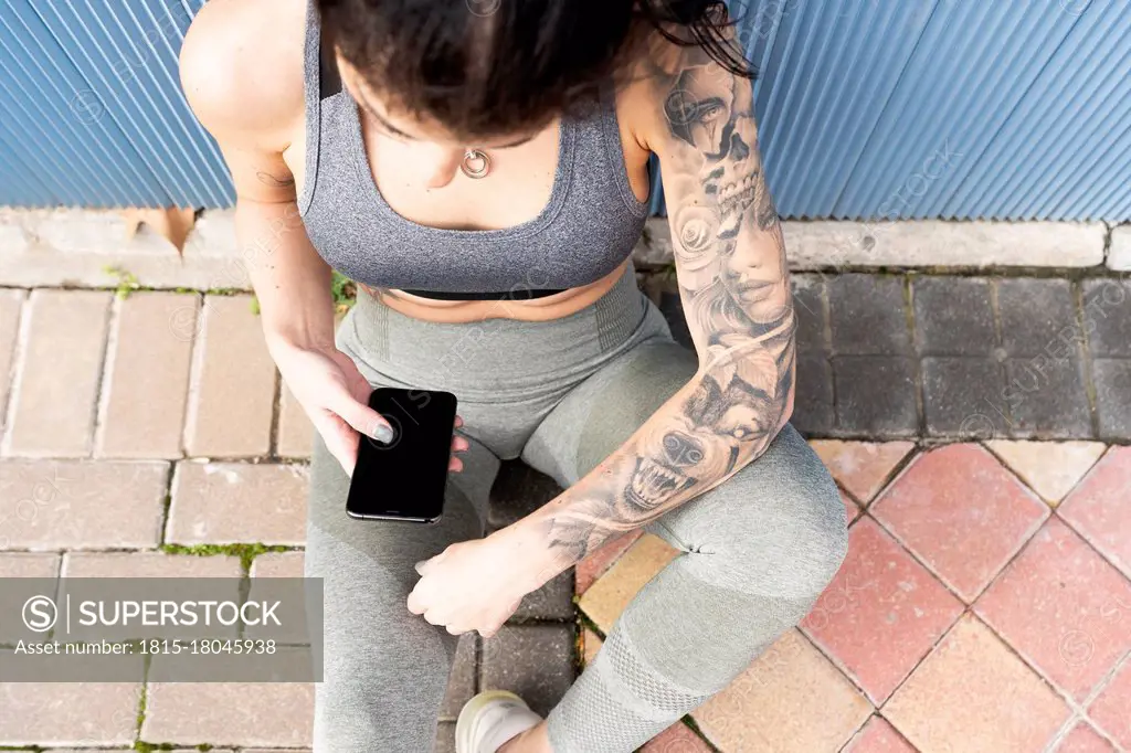 Mid adult woman using mobile phone while sitting on footpath