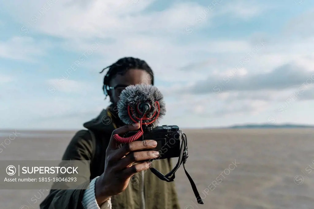 Young traveler making vlog of himself at beach against sky