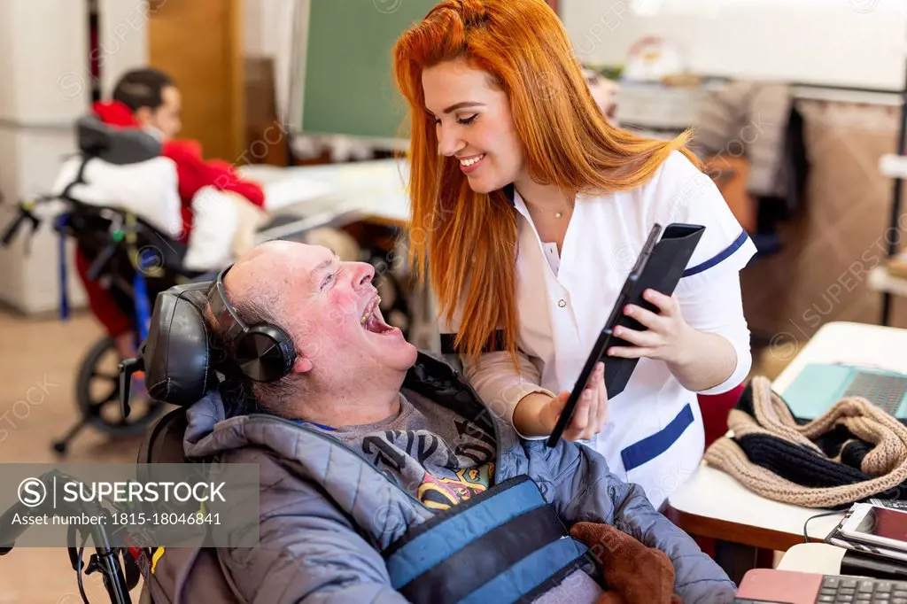 Smiling nurse showing digital tablet to happy disabled man in nursing home