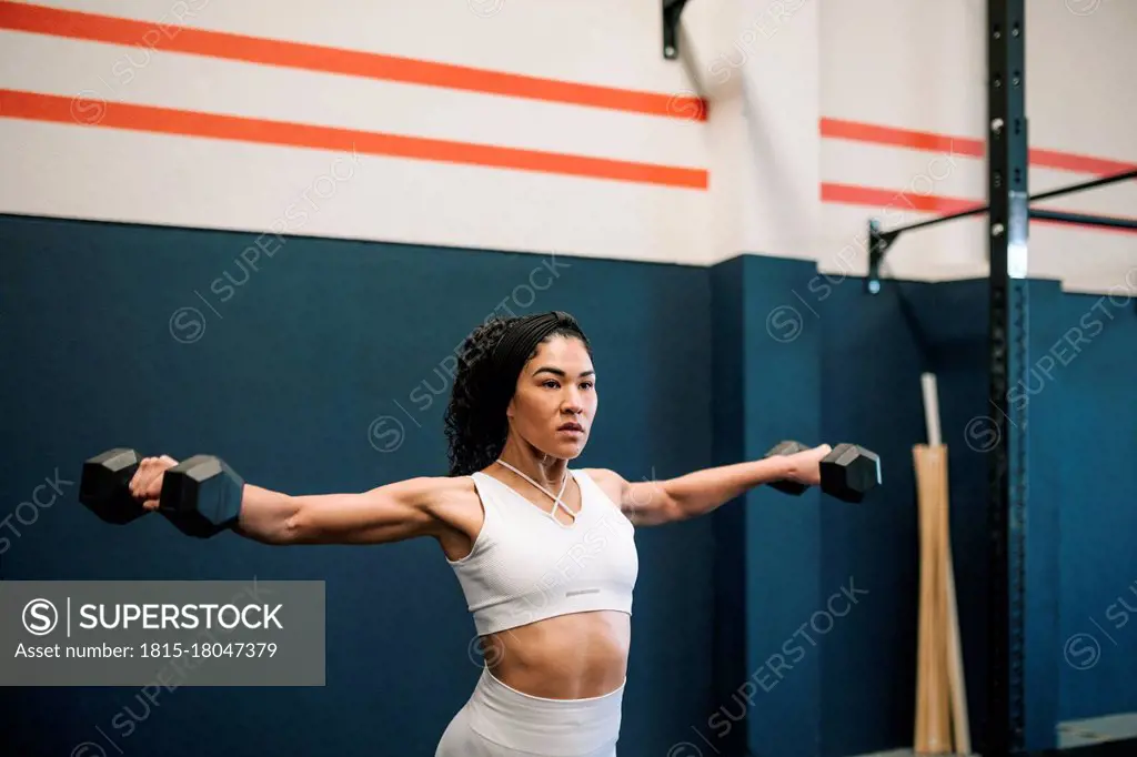 Female athlete working out with dumbbells against wall in gym