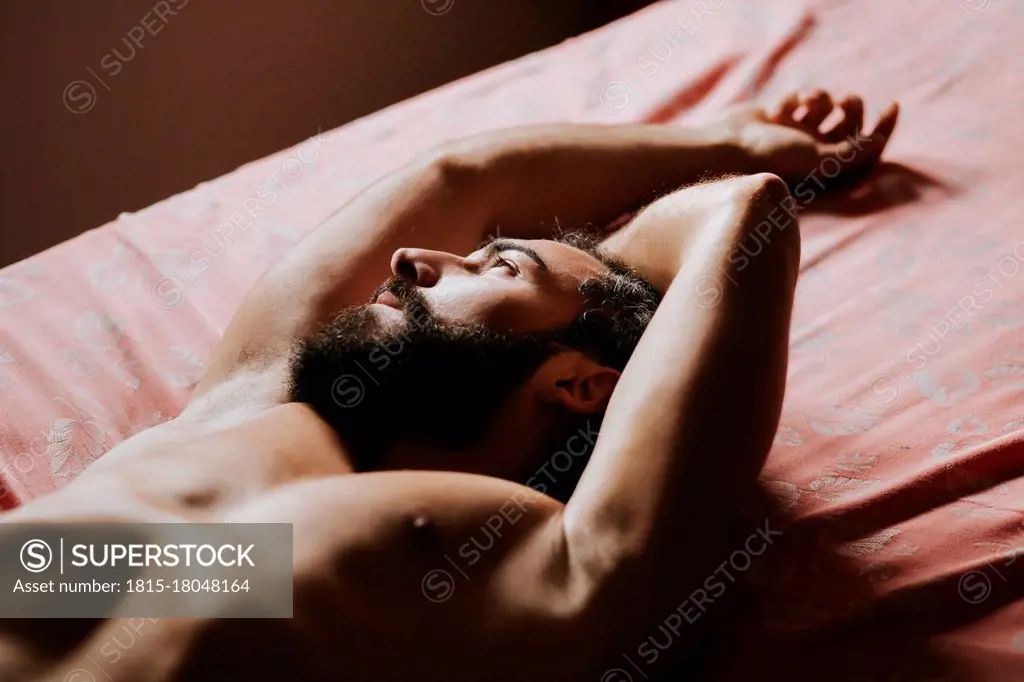 Young shirtless man resting in bedroom at home