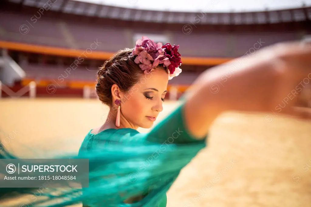 Close-up of flamenco dancer wearing flowers with eyes closed dancing in bullring