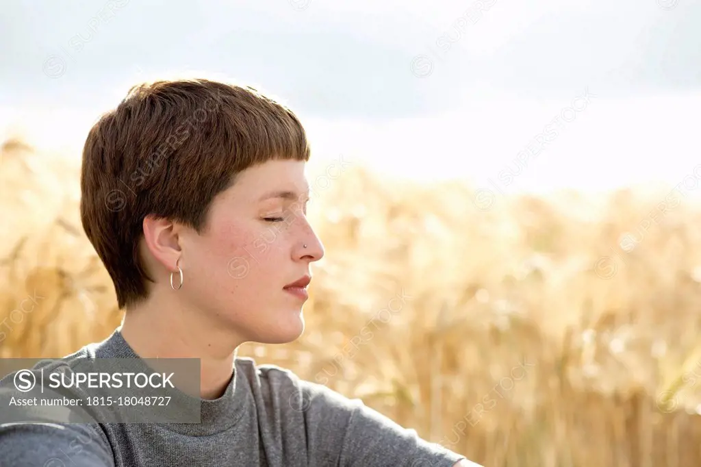 Woman sitting at crop plant field on sunny day