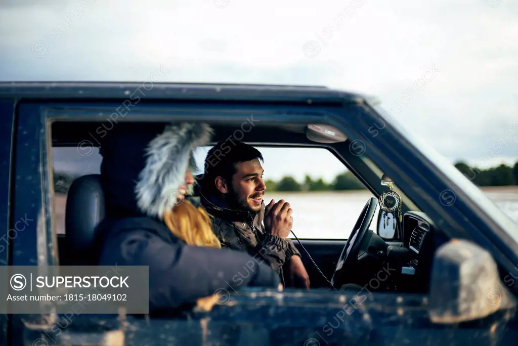 Young man using CB radio while traveling with female friend in car during winter