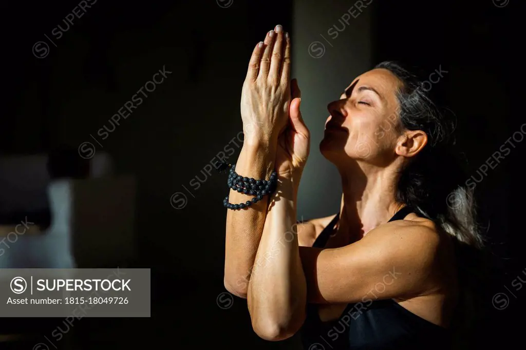 Yogini with eyes closed doing twisted arms meditation in living room in sunlight