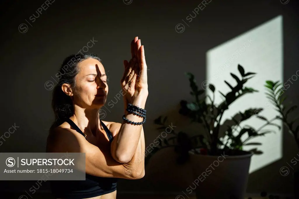 Yogini meditating with eyes closed in living room on sunny day