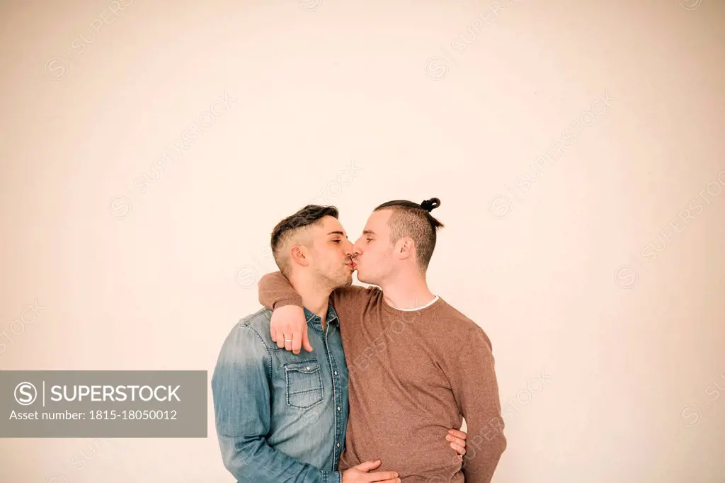 Affectionate gay couple kissing against beige background