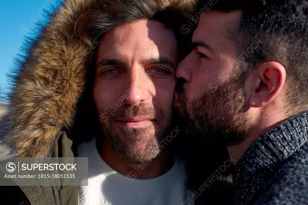 Close-up of man kissing on boyfriend's cheek wearing hood