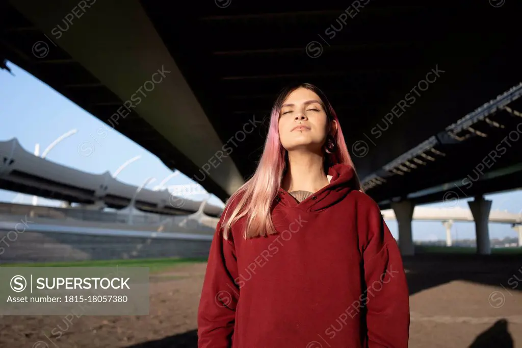 Young woman with eyes closed below bridge on sunny day